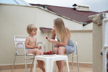 Caucasian family eat strawberries in summer sitting on the terrace on the background of the roofs