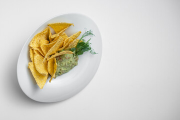 closeup of guacamole dip in bowl with avocado and nachos on white background
