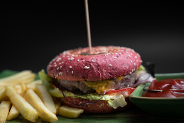 closeup of fresh tasty red burger wit french fries and sauce on black background