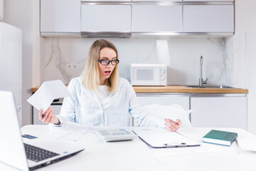 young female housewife sitting a table in house kitchen an incomprehensible deal with paperwork bills and loans. Woman is exhausted and frustrated with documents of enterprise or family budget at home