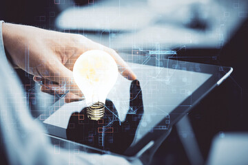 Double exposure of man's hands holding and using a digital device and bulb hologram drawing. Idea concept.