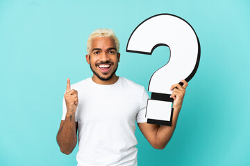 Young Colombian handsome man isolated on blue background holding a question mark icon