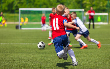 Obraz na płótnie Canvas Group of Soccer Boys in Red Uniforms Playing School Tournament Game. Child Football Team Captain Running Ball and Compete in a Duel