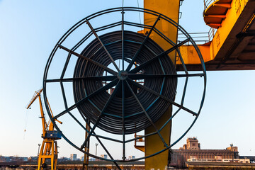 A large wheel with a harbor crane electric cable coiled around it in the port area.