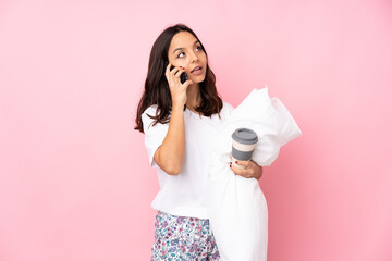 Young woman in pajamas isolated on pink background holding coffee to take away and a mobile