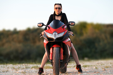 Fototapeta premium A direct view of a girl with braided pigtails sitting on a red motorbike. Selective focus.