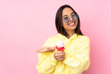 Young brunette girl holding a cornet ice cream over isolated pink background presenting an idea while looking smiling towards