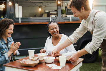 Multiracial women eating at food truck restaurant outdoor - Focus on african woman face