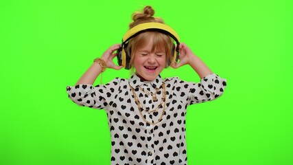 Attractive blonde child kid 5-6 years old listening music via headphones, dancing disco fooling around having fun expressive gesticulating hands. Teenager children girl on chroma key green background