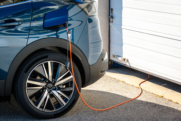 A hybrid electric car parked in front of the home garage door is plugged in with a charging cable...