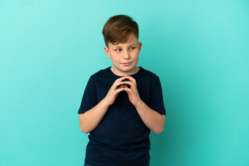 Fototapeta premium Little redhead boy isolated on blue background scheming something