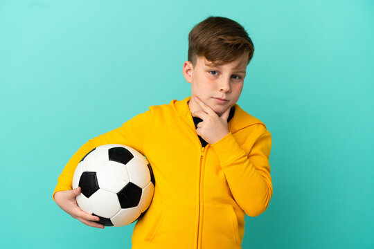 Redhead kid playing football isolated on blue background thinking