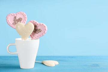 Heart shaped lollipops made of chocolate on light blue background, space for text
