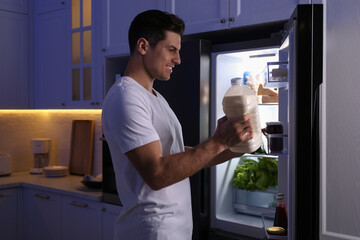 Naklejka na ściany i meble Man holding gallon bottle of milk near refrigerator in kitchen at night
