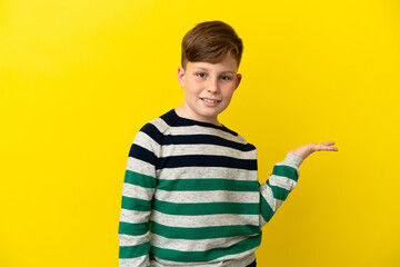 Little redhead boy isolated on yellow background holding copyspace imaginary on the palm to insert an ad