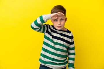 Little redhead boy isolated on yellow background looking far away with hand to look something
