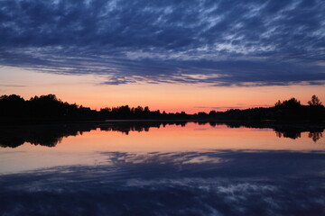 A beautiful Russian landscape orange sunset on the Volga River with a reflection of blue clouds in the sky in the calm water and a forest on the horizon on a summer evening