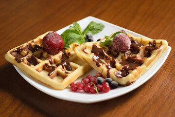 Two large waffles poured with chocolate, with frozen strawberries and berries on a white plate