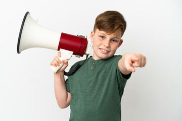 Little redhead boy isolated on white background holding a megaphone and smiling while pointing to...