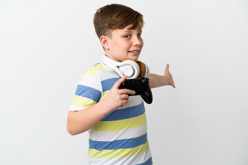 Fototapeta premium Little redhead boy holding a game pad isolated on white background extending hands to the side for inviting to come