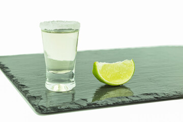 Shot glass with tequila and lime on a white background