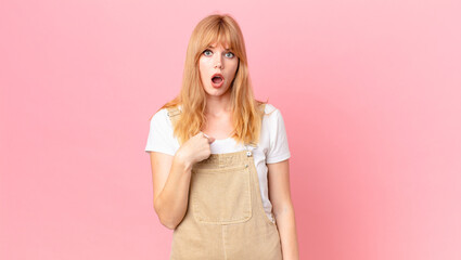 pretty red head woman looking shocked and surprised with mouth wide open, pointing to self