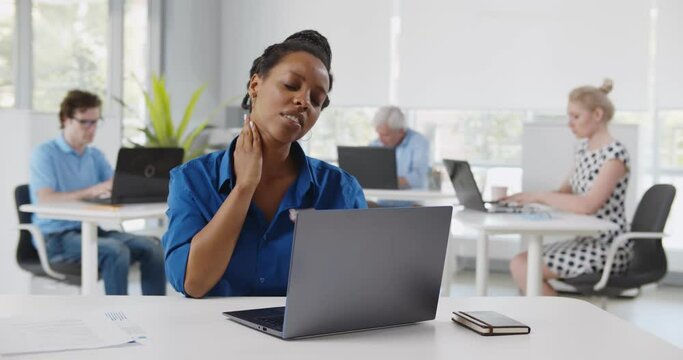 African young woman suffering with pain massaging neck while working in office