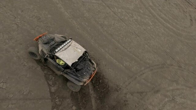 Brutal buggy automobiles drift on dried salt lake territory with brown sand leaving circle traces against hill silhouettes. Aerial view on sport fpv drone