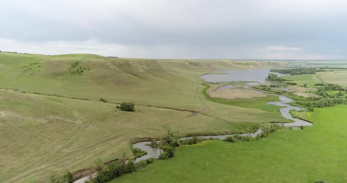 Source of the river with beauty calm swampy backwater with reeds and thickets and bald hills background. Aerial above drone wide view at summer cloudy day.
