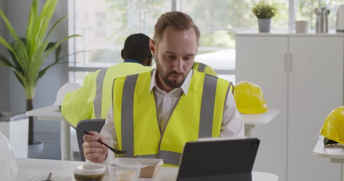 Construction company worker in reflective vest having lunch and using digital tablet in canteen