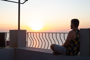 man hipster relaxing on the roof or balcony and looking on sunrise or sunset near sea