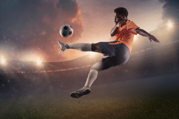 Fototapeta na wymiar Male soccer, football player kicking ball in jump at the stadium during sport match on dark sky background