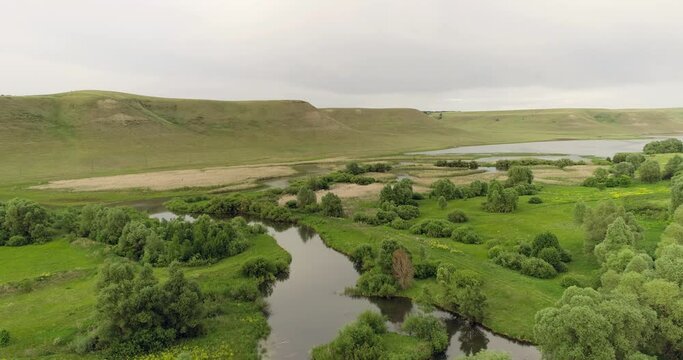 Source of the river with beauty calm swampy backwater with reeds and thickets and bald hills background. Aerial above drone wide view at summer cloudy day.