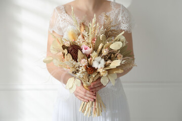 Bride holding beautiful dried flower bouquet at home, closeup