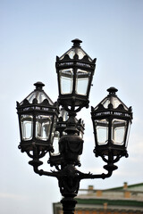 Fototapeta na wymiar Black metal street triple lamp. Old lamp and blue sky .