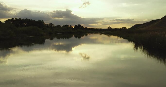Source of the river with beauty calm swampy backwater with reeds and thickets and bald hills background. Aerial above drone wide view at summer evening sky.