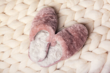 Home slippers made of fur on the background of white merino wool plaid. The atmosphere of homeliness and comfort.