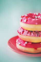 Delicious bright cute pink donuts with sprinkles in the form of hearts are lying on a red saucer. A romantic and appetizing gift for the Valentine's holiday. Love and food.