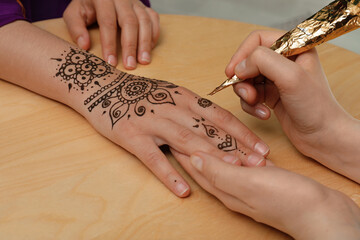 Master making henna tattoo on hand at wooden table, closeup. Traditional mehndi