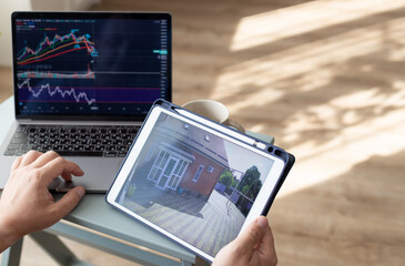 Close-up person hands holding digital tablet with home security camera and working on laptop. multi-tasking, freelance and home office concept. copy space