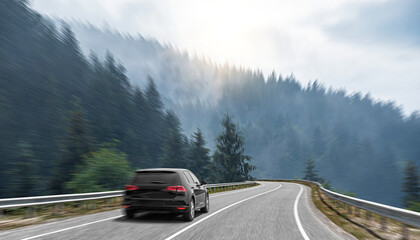 A black car rushes along the road against the backdrop of a beautiful landscape.