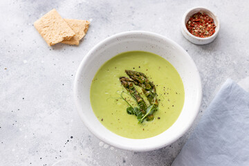 green soup with asparagus and coconut milk in white bowl on gray background. Healthy vegan food concept. copy space