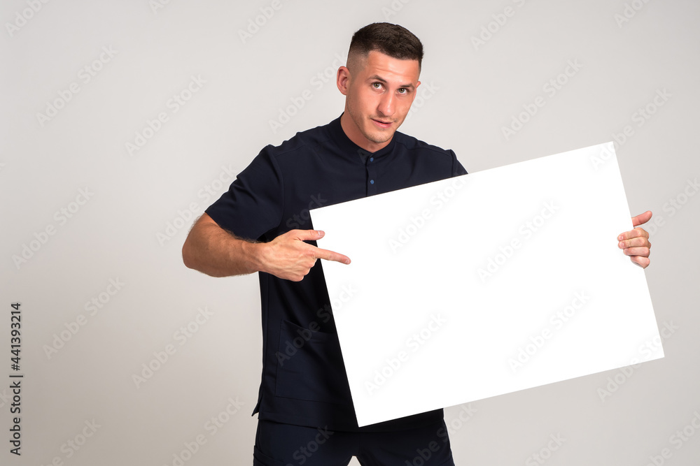 Poster man points to blank banner. brunet guy on gray background. businessman with a place to write on blan