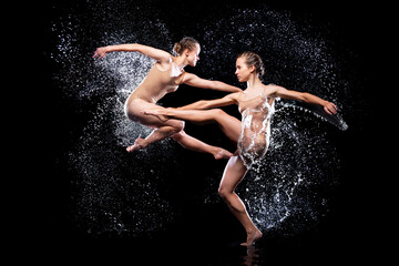Fototapeta na wymiar Couple of athletic women are doing dancing tricks under streams, splashes, drops of rain water. Duo acrobats, ballet dancers are performing dance. Freedom and freshness concept. Modern art and beauty.