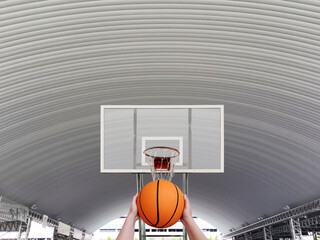 Hand holding a basketball The old basketball hoop is in a large dome. front view. indoor sports