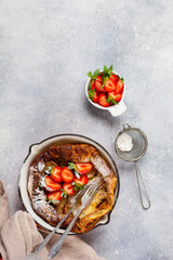 Dutch baby pancake with fresh strawberry berry and sprinkled with icing sugar powder in red pan on white kitchen background. Top view