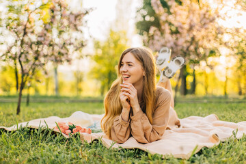 smiling young woman, with a bouquet of pink tulips in a straw hat, sits on the lawn in a blooming sakura garden