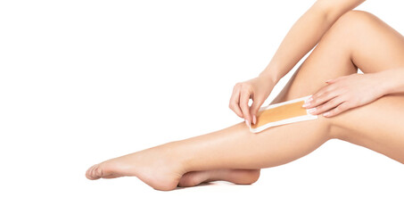 Beautician waxing female legs in spa center. Well-groomed woman legs after depilation isolated on white background. Waxing woman leg with wax strip at beauty spa. Close-up waxing woman leg in spa - obrazy, fototapety, plakaty
