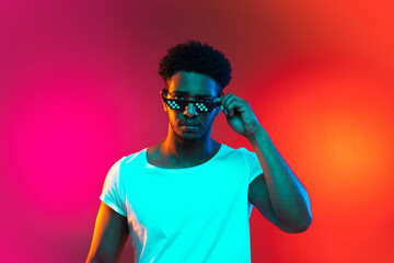 Portrait of young african man at studio on bright pink neon background. Concept of emotions and...