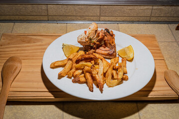 Homemade grilled chicken served on a ceramic white plate with with rustic fried potatoes and sauce. Isolated over wooden board.